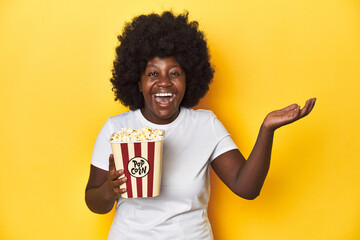 Movie night concept with woman holding popcorn receiving a pleasant surprise, excited and raising...