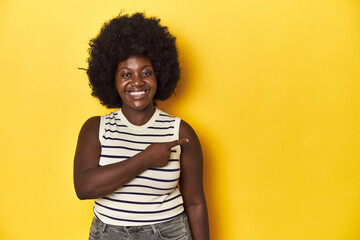 Fototapeta na wymiar African-American woman with afro, studio yellow background smiling and pointing aside, showing something at blank space.