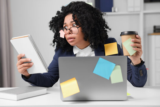 Deadline concept. Stressed woman looking at notepad and holding paper cup in office. Many sticky notes everywhere as reminders