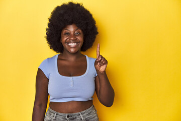 African-American woman with afro, studio yellow background showing number one with finger.