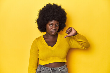 Fototapeta na wymiar African-American woman with afro, studio yellow background showing thumb down, disappointment concept.