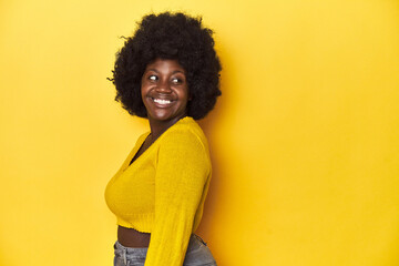 Fototapeta na wymiar African-American woman with afro, studio yellow background looks aside smiling, cheerful and pleasant.