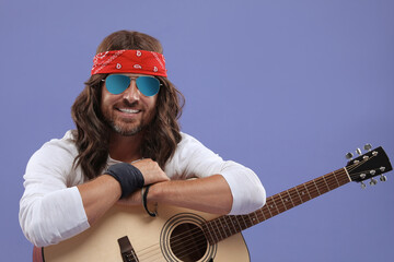 Stylish hippie man with guitar on violet background