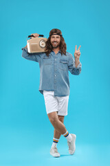 Stylish hippie man with retro radio receiver showing V-sign on light blue background
