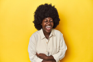 Fototapeta na wymiar African-American woman with afro, studio yellow background laughing and having fun.