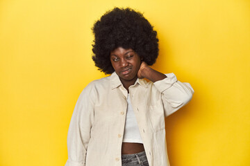 Fototapeta na wymiar African-American woman with afro, studio yellow background having a neck pain due to stress, massaging and touching it with hand.