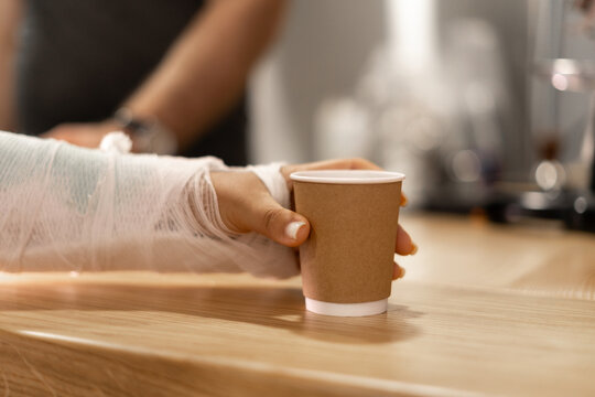 Close-up of a woman with a broken arm in a cast taking coffee to go in a cafe