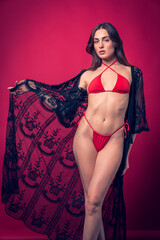 Fototapeta premium Studio photo shoot of beautiful brown hair model posing wearing red swimwear with red background behind