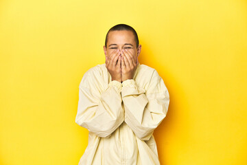 Fototapeta premium Young woman in jacket, yellow studio backdrop laughing about something, covering mouth with hands.