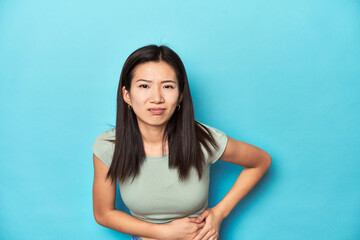 Asian woman in summer green top, studio backdrop, having a liver pain, stomach ache.