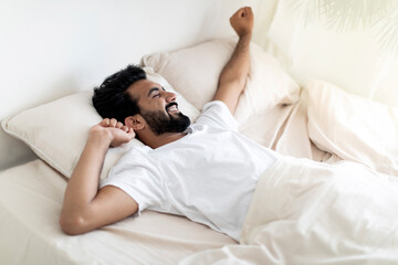 Handsome Young Indian Man Stretching Hands While Lying In Comfortable Bed