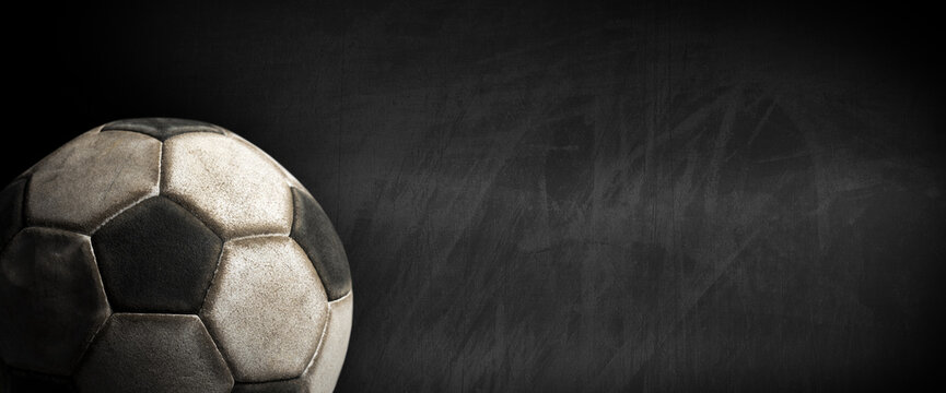 Closeup of an old leather soccer ball on a blank blackboard with copy space.