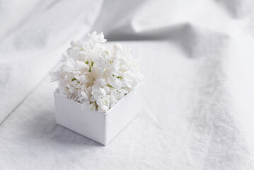Close-up of a bouquet of white flowers in a white gift box on a white textile background. Slow life concept. Greeting card mockup	