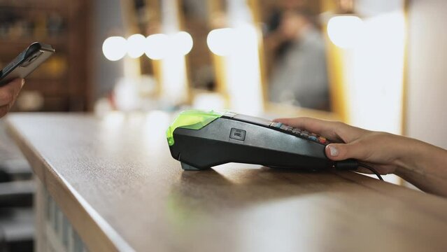 Unrecognisable man using smartphone cashless electronic wallet NFC technology to pay for order on bank pos terminal at store, beauty salon, restaurant. Contactless payment. E-money transfer