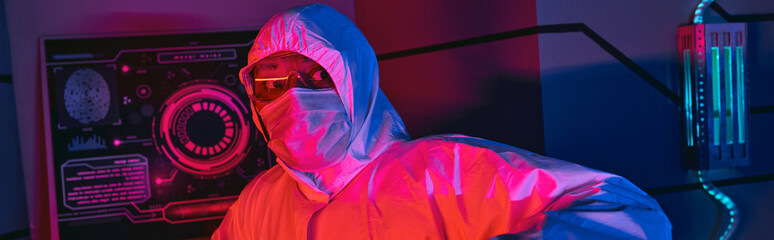 indian scientist in hazmat suit, goggles and medical mask looking away in science center, banner