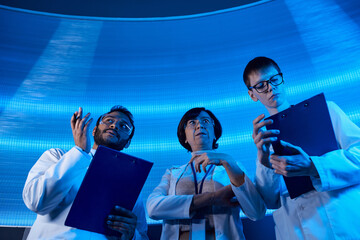 indian scientist pointing with hands near colleagues in science center, future-oriented