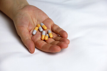 Pills in a palm of female hand on the bed. Concept of medication, vitamins or sleeping pill