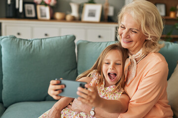 Happy grandmother and granddaughter taking selfie using smartphone in the living room