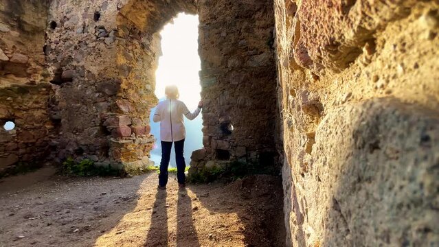 Wide angle 4K video shot of warm clothed tourist woman enjoying the sunset sun light in medieval Slovakian castle ruins during autumn nature walk. Stary Hrad Strecno, Zilina, Slovakia.