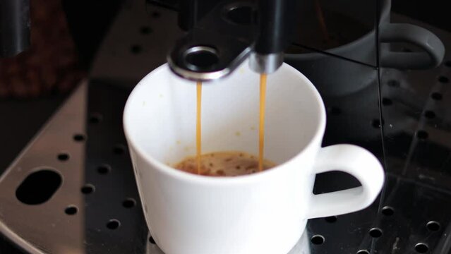 A modern coffee machine pours delicious coffee into a white cup standing on a metal support, close-up. Coffee.