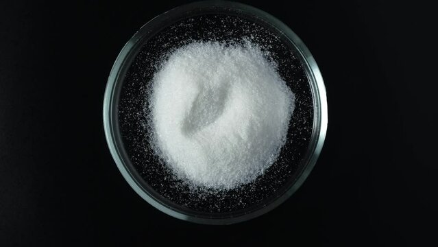 Trisodium citrate powder in Petri dish on dark background, top view. Food additive E331. Preservative and flavoring. Acidity regulator, emulsifier, complexing agent.