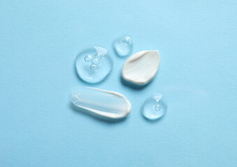 Samples of transparent gel and white cream on light blue background, flat lay