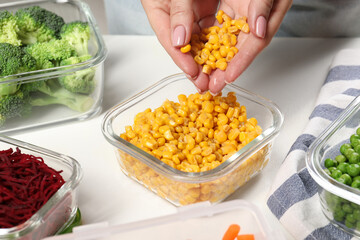 Woman putting corn into glass container at white table, closeup. Food storage
