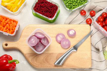 Wooden board with cut onion, knife and containers with fresh products on light gray table, flat lay. Food storage