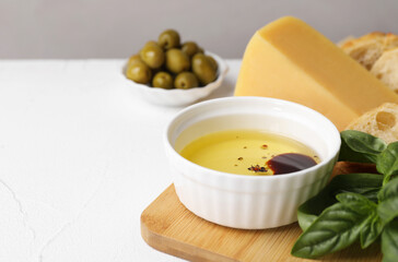 Bowl of organic balsamic vinegar with oil, basil, bread and cheese on white table, space for text