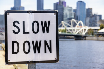 Slow Down sign on the Yarra river in Melbourne, Australia, on a summer day with city buildings and...
