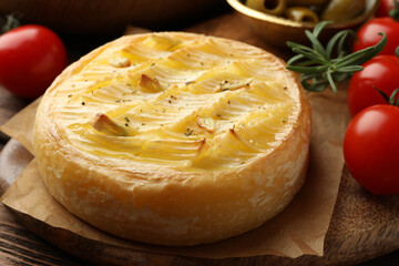 Tasty baked brie cheese with rosemary and cherry tomatoes on wooden board, closeup