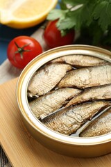 Tin can with tasty sprats served on wooden board, closeup