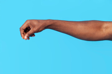 african american male hand pours spices and salts on blue isolated background, the hand holds pinch