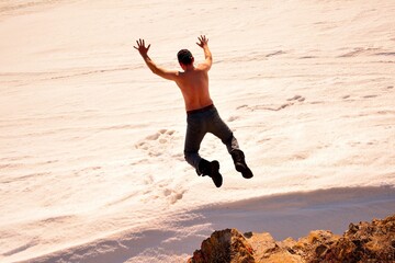 Crazy man jump off the rocks cliff into white snow. 
