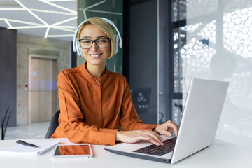 Portrait of successful smiling female programmer, female worker looking at camera using laptop to...