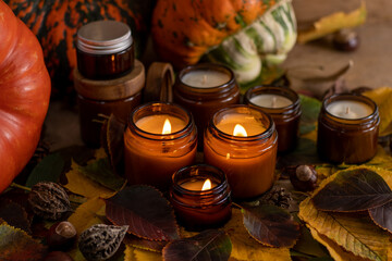 Obraz na płótnie Canvas Soy candles burn in glass jars. Tree leaves, pumpkin. Comfort at home. Candle in a brown jar. Scent and light. Scented handmade candle. Aroma therapy. Autumn mood. Cozy home decor in fall.