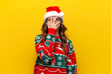 facepalm gesture. puzzled girl in christmas sweater and santa claus hat covers her face with her hand