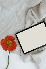 Flatlay of blank screen tablet pad with mockup copy space and poppy flower on crumpled fabric. Aesthetic social media template. Flat lay, top view