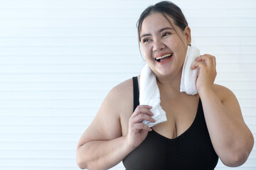 Overweight woman wipes sweat after exercising with white towel, feeling refreshed, smiling and...