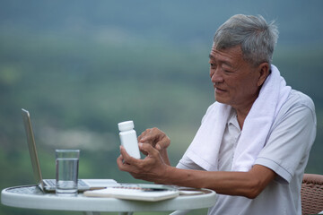 Asian old man is feeling unwell, like having a fever after exercising, sitting and holding medicine...