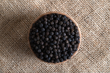 Black peppercorns in wooden bowl on burlap sack