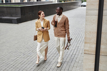 Young businessman with skateboard describing his point of view or explaining something to female colleague on their way to work