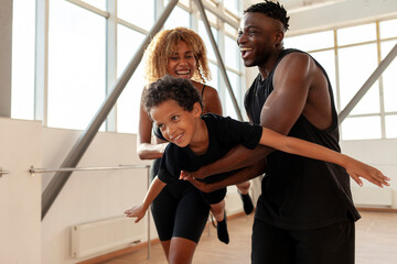 athletic african american family in sportswear holding and carrying son in the air and playing in...