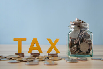 Tax wooden letter on stacked coins with coin in glass jar. Tax deduction planning concept....