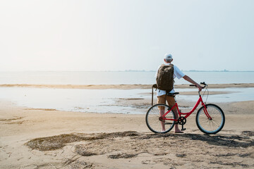 rear view of man with backpack standing and holding bike on seafront
