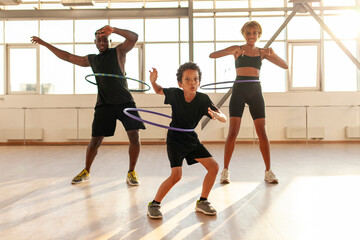 sporty african american family in sports uniform twists hula hoop and does exercises in the gym