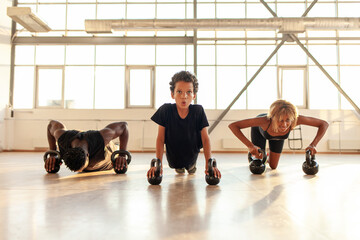 athletic african american family in sportswear train and play sports in the gym, the boy with his parents do push-ups