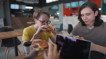 a group of students lifestyle sit in a cafe and do a project on a laptop together. business concept of modern training and development. students discuss their homework and eat fast food burgers