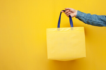 empty fabric eco bag on a yellow background, the guy's hand holds a reusable non-plastic bag