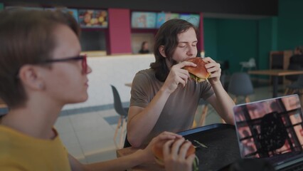 a group of students sit in a cafe and do lifestyle a project on a laptop together. business concept of modern training and development. students discuss their homework and eat fast food burgers